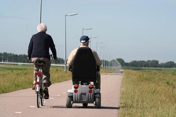 A man riding a bicycle and man driving a motorized wheelchair down a country road