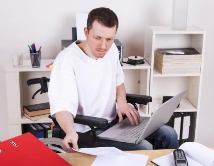 male wheelchair user at a desk, working on a laptop